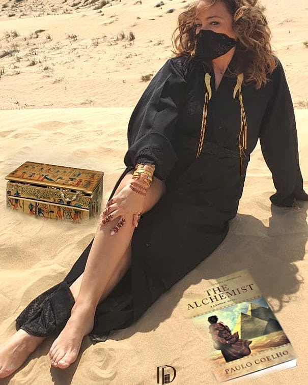 Diala Arslan in the desert sands of Dubai with The Alchemist by Paul Coelho