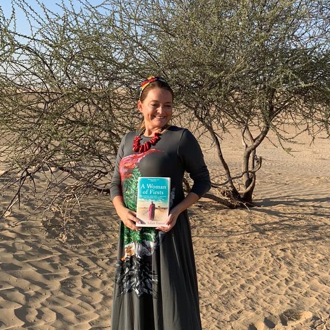 Diala Arslan in the sands of Dubai with the book A Woman of Firsts by Edna Adan Ismail